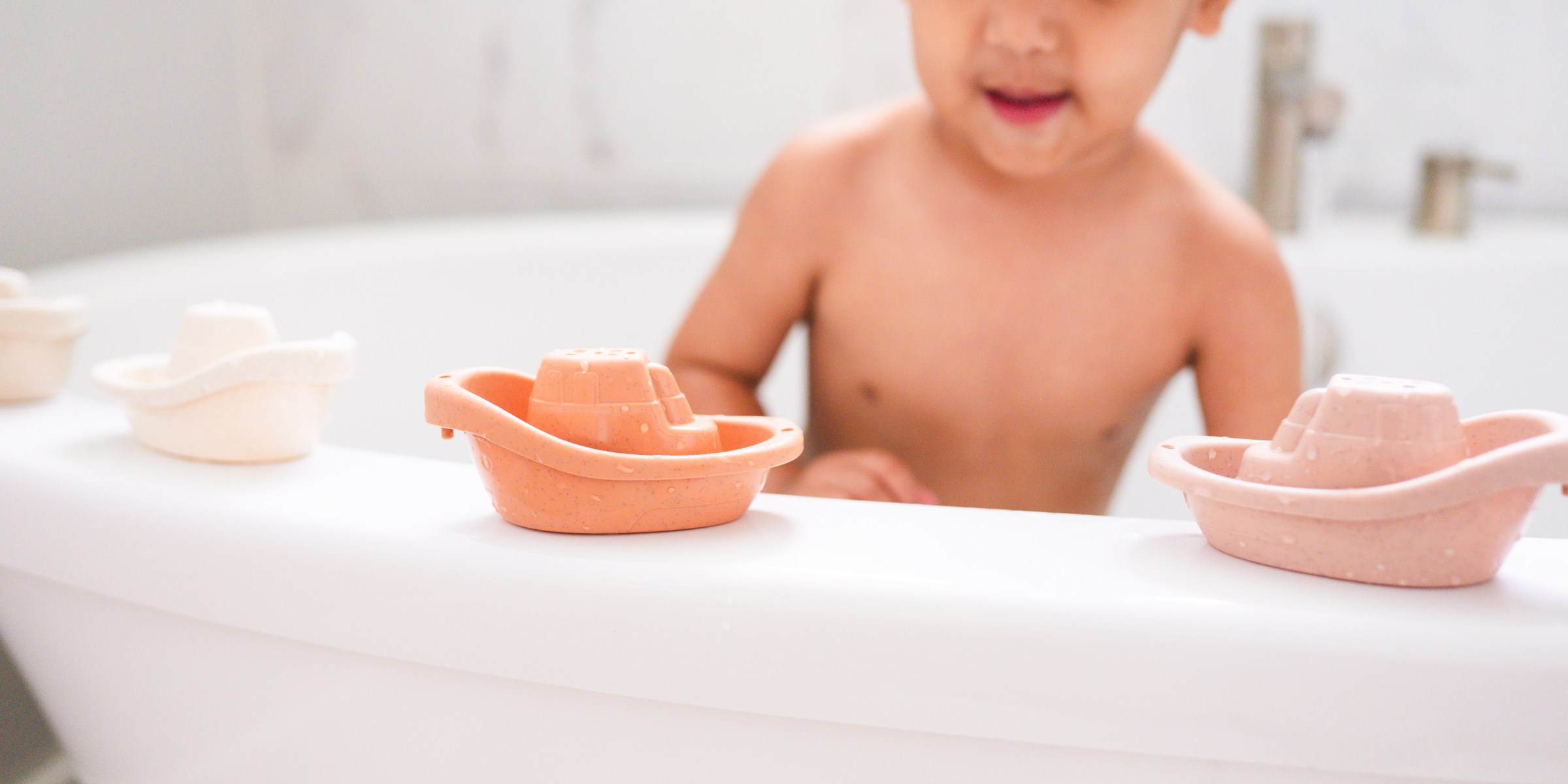 Child playing with eco-friendly wheat straw boat set in bathtub; sustainable, biodegradable fun by Bug + Bean Kids.