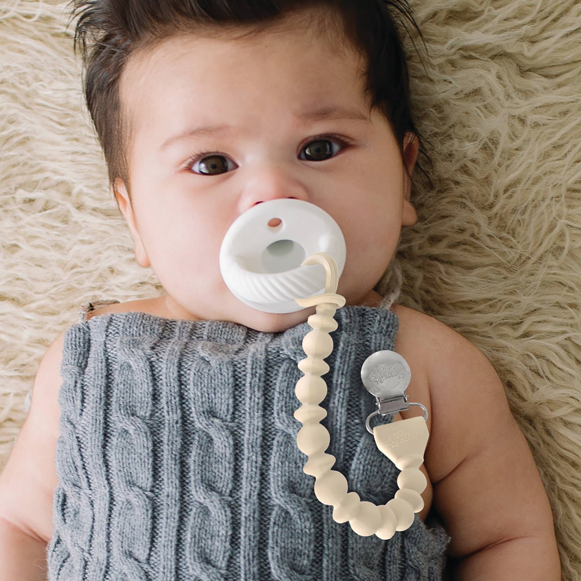 Cute baby using Sweetie Strap™ silicone pacifier clip with braided design, keeping pacifier secure and stylish.