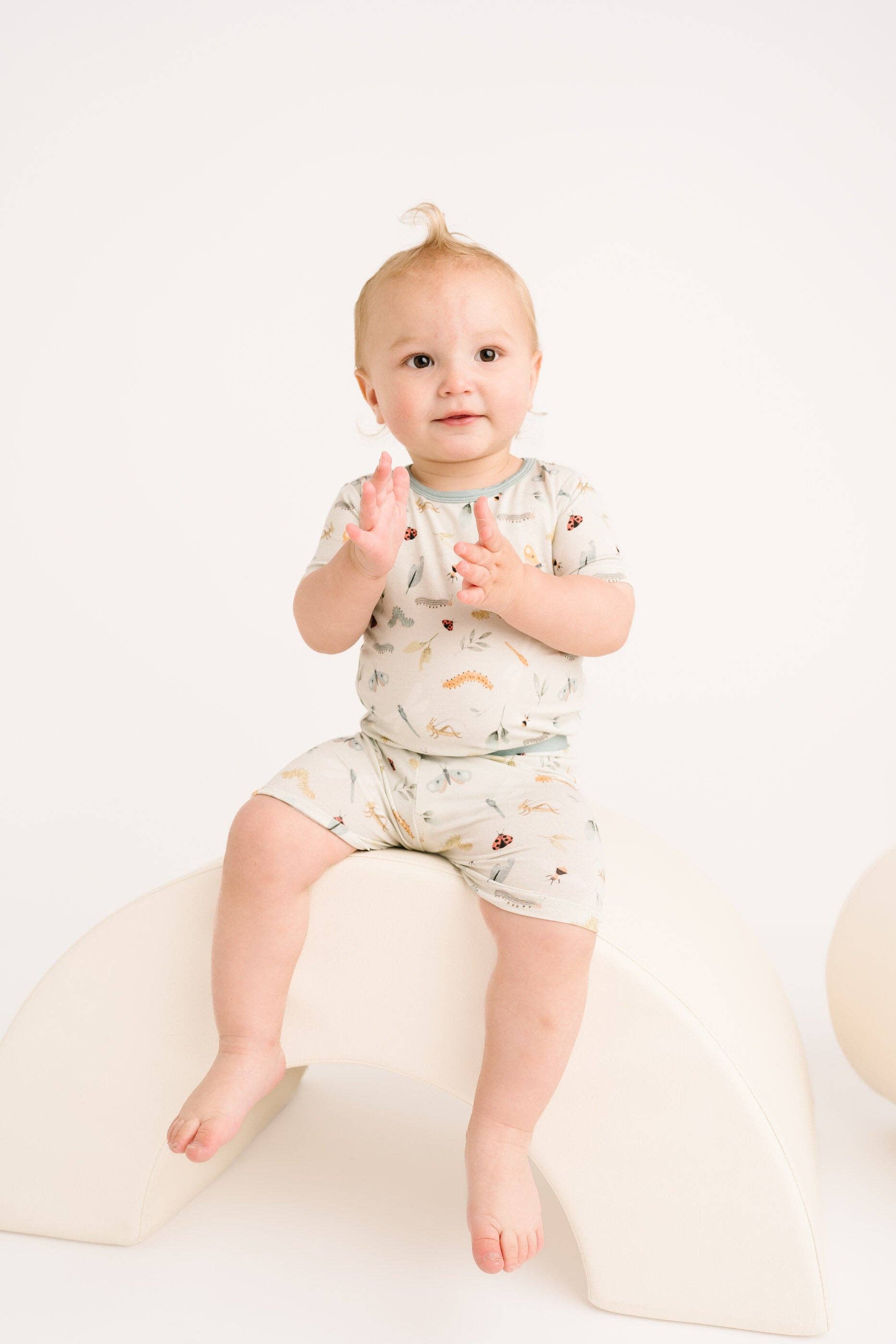 Baby in Bug Buddies Bamboo Shorts Set, 12-18 months, sitting on a curved white block, wearing comfy and stylish bamboo blend attire.