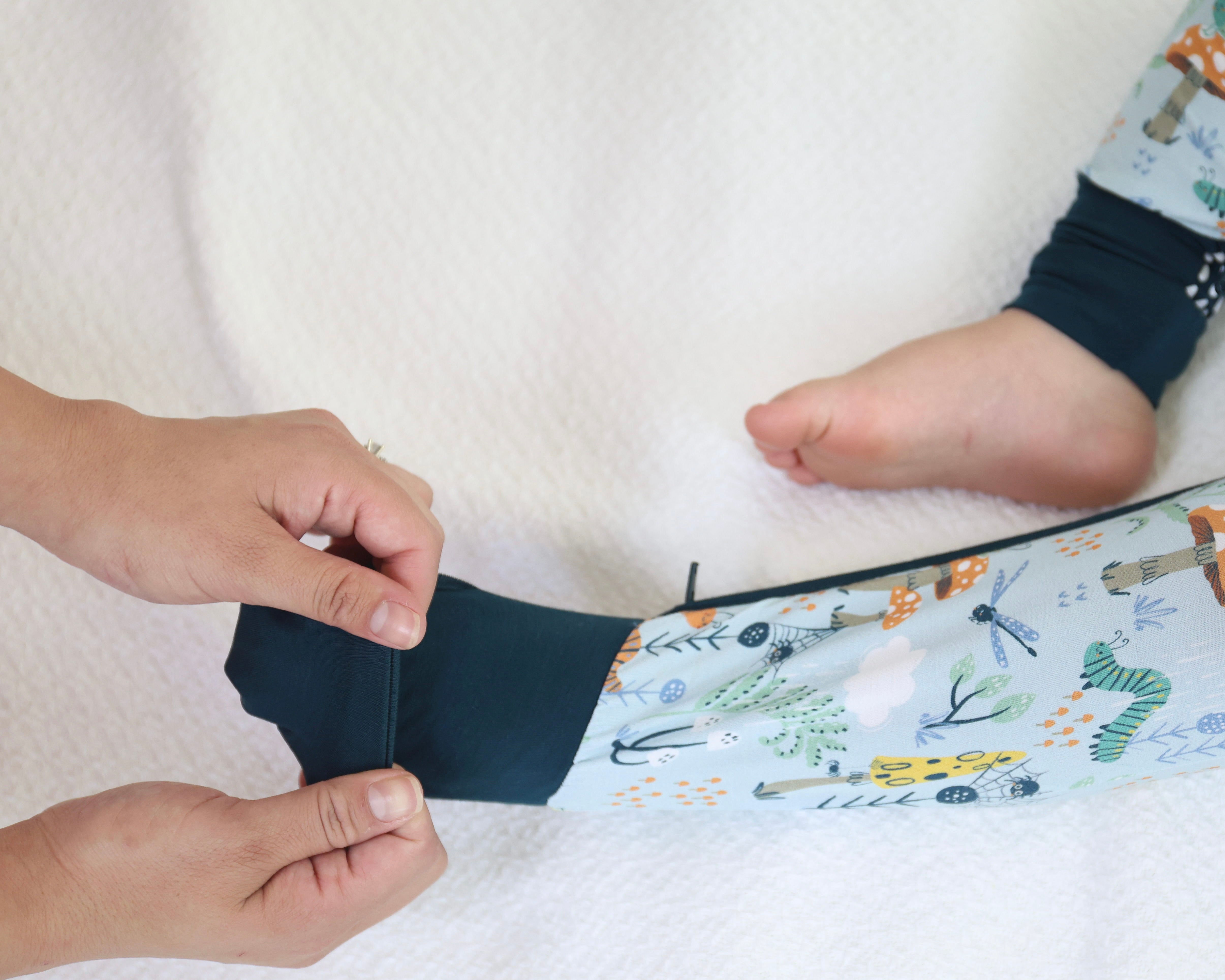 Parent putting on Bamboo Zipp Jammies with Critter Hollow design on baby's leg, emphasizing soft, breathable, hypoallergenic comfort.