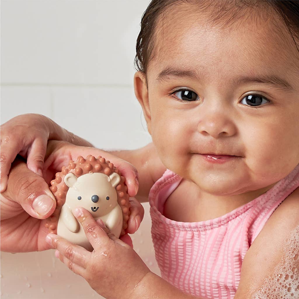 Baby playing with soft Itzy Squirt™ hedgehog bath toy during bath time fun.