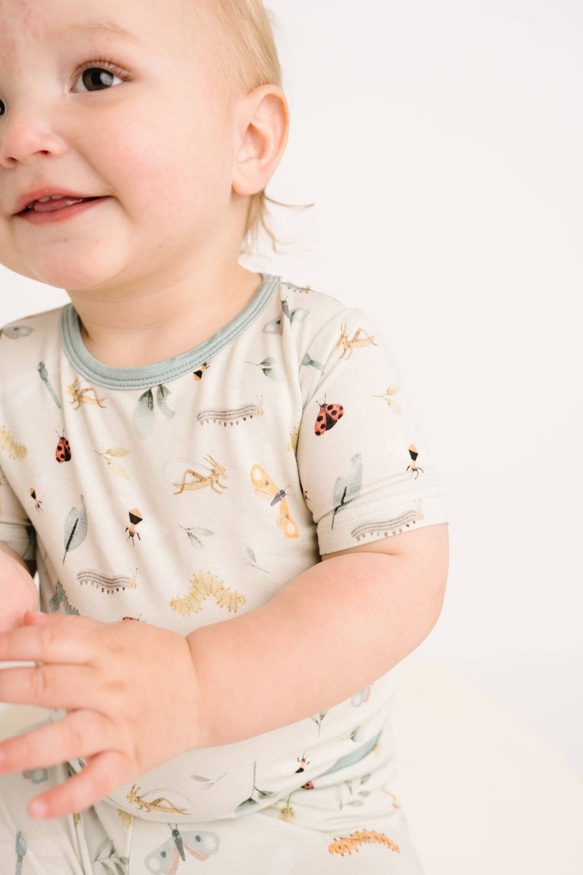 Smiling toddler wearing Bug Buddies Bamboo Shorts Set from Little One Shop, showcasing insect print and soft bamboo fabric.
