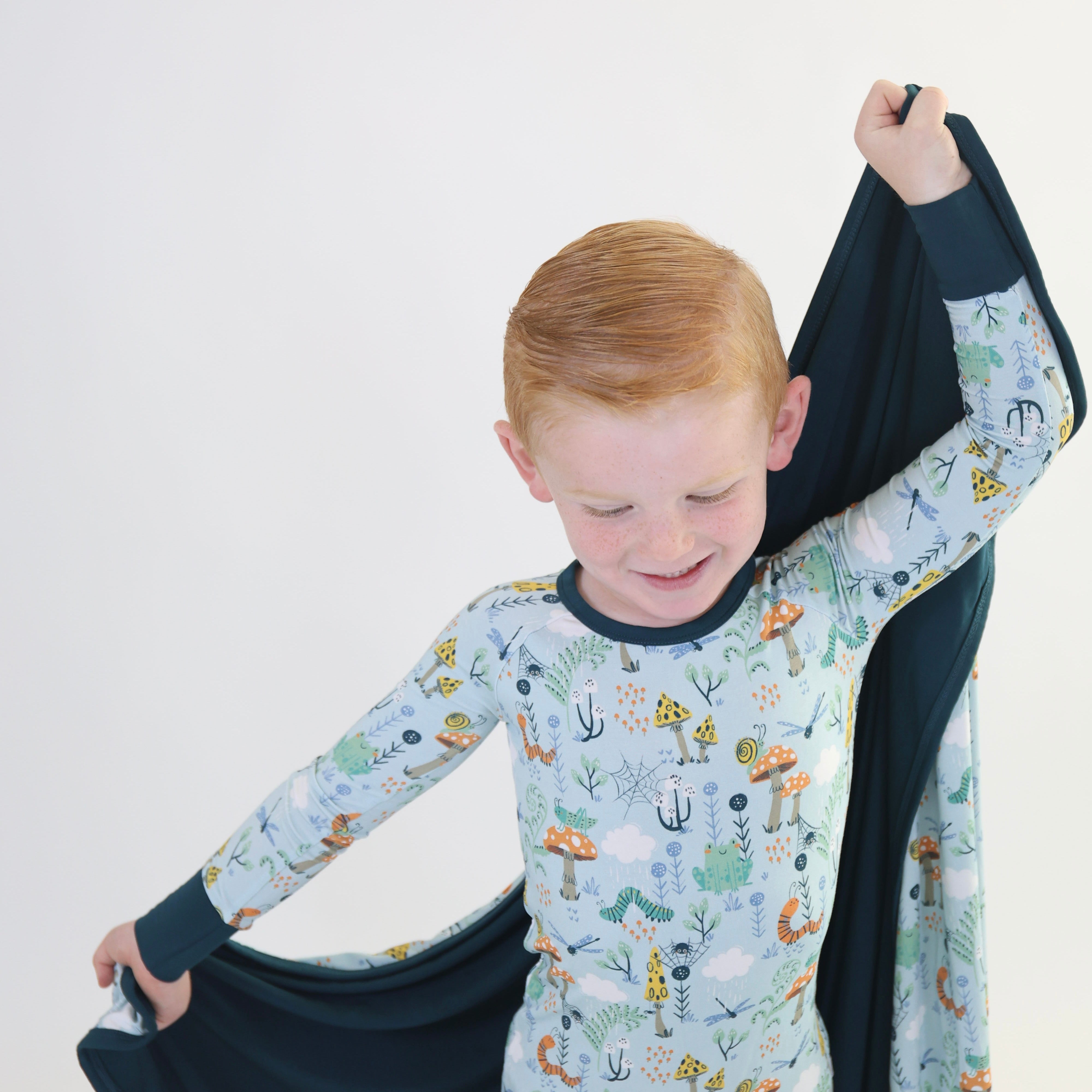 Happy boy in colorful pajamas playfully holding a cozy Rainn blanket, showcasing fun nature patterns.