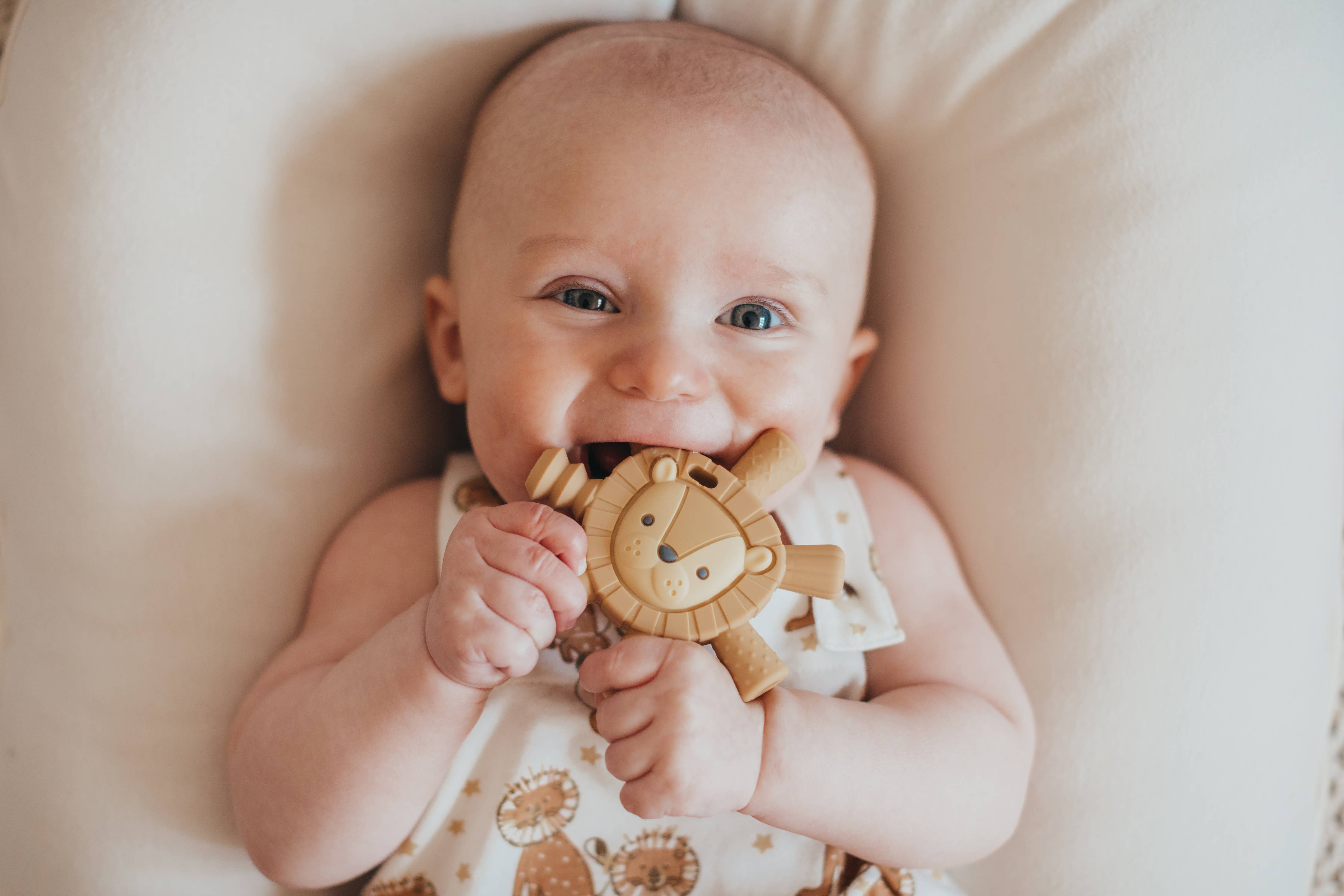 Smiling baby holding Itzy Ritzy Lion teether for soothing teething relief and eco-friendly comfort.