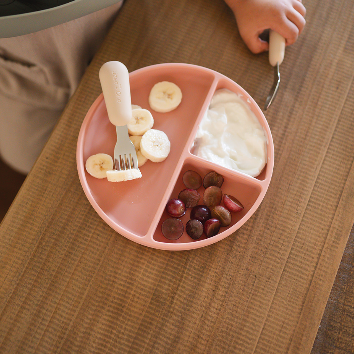 Child's pink plate filled with banana slices, grapes, and yogurt, perfect for toddler mealtime.
