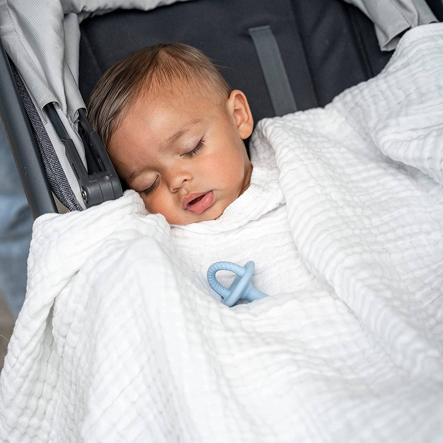 Baby sleeping peacefully in a stroller, bundled in a cozy Comfy Cubs muslin cotton blanket.