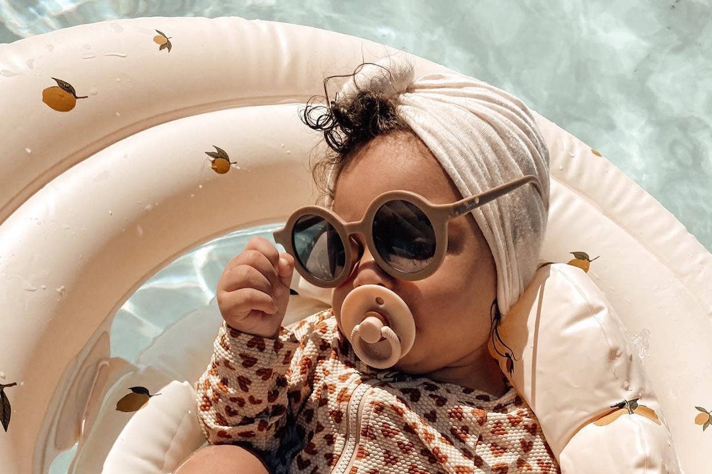 Cute baby in sunglasses enjoying the pool, relaxing with an Itzy Soother™ Natural Rubber Pacifier.