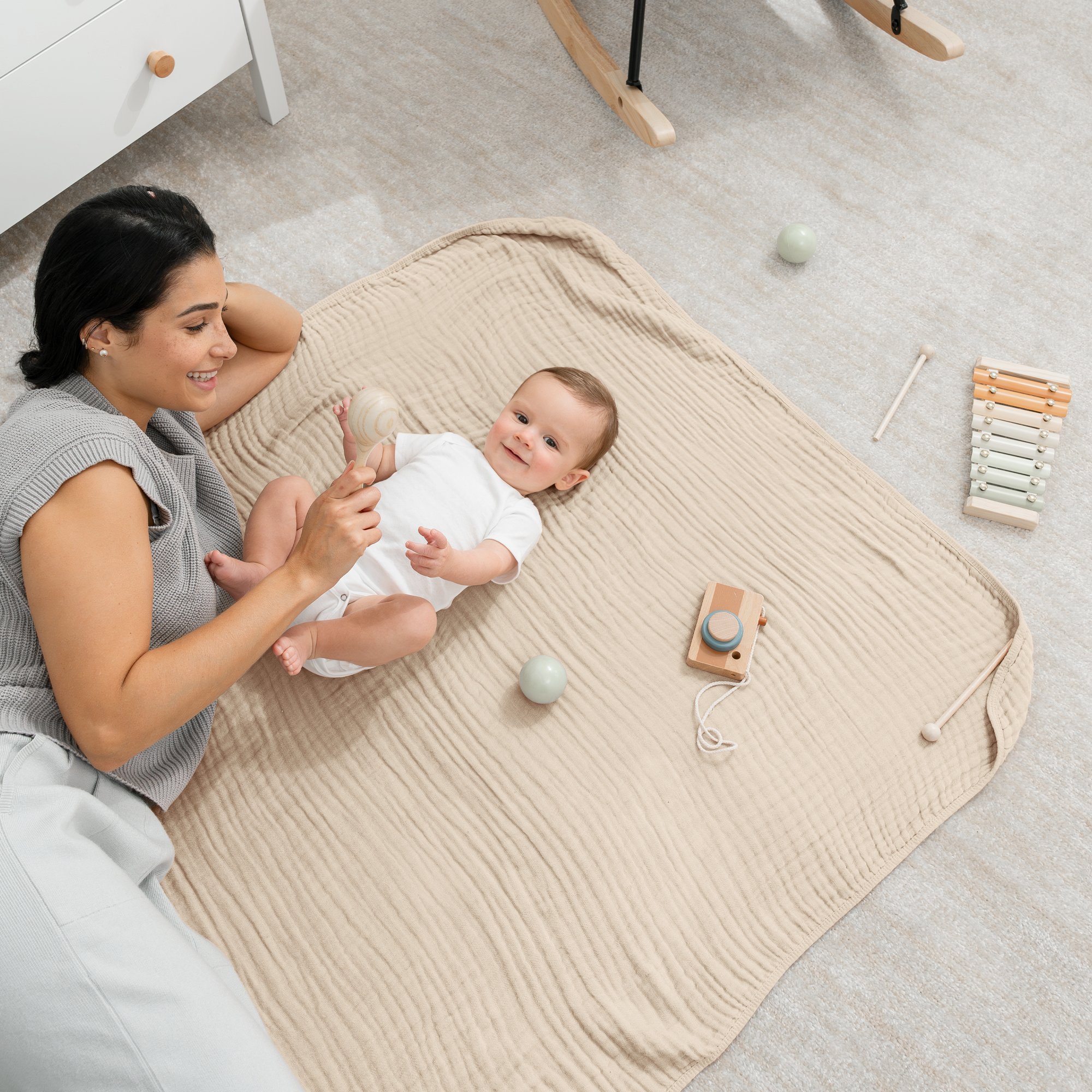 Mother playing with baby on cozy muslin cotton blanket, promoting comfort and bonding during playtime.