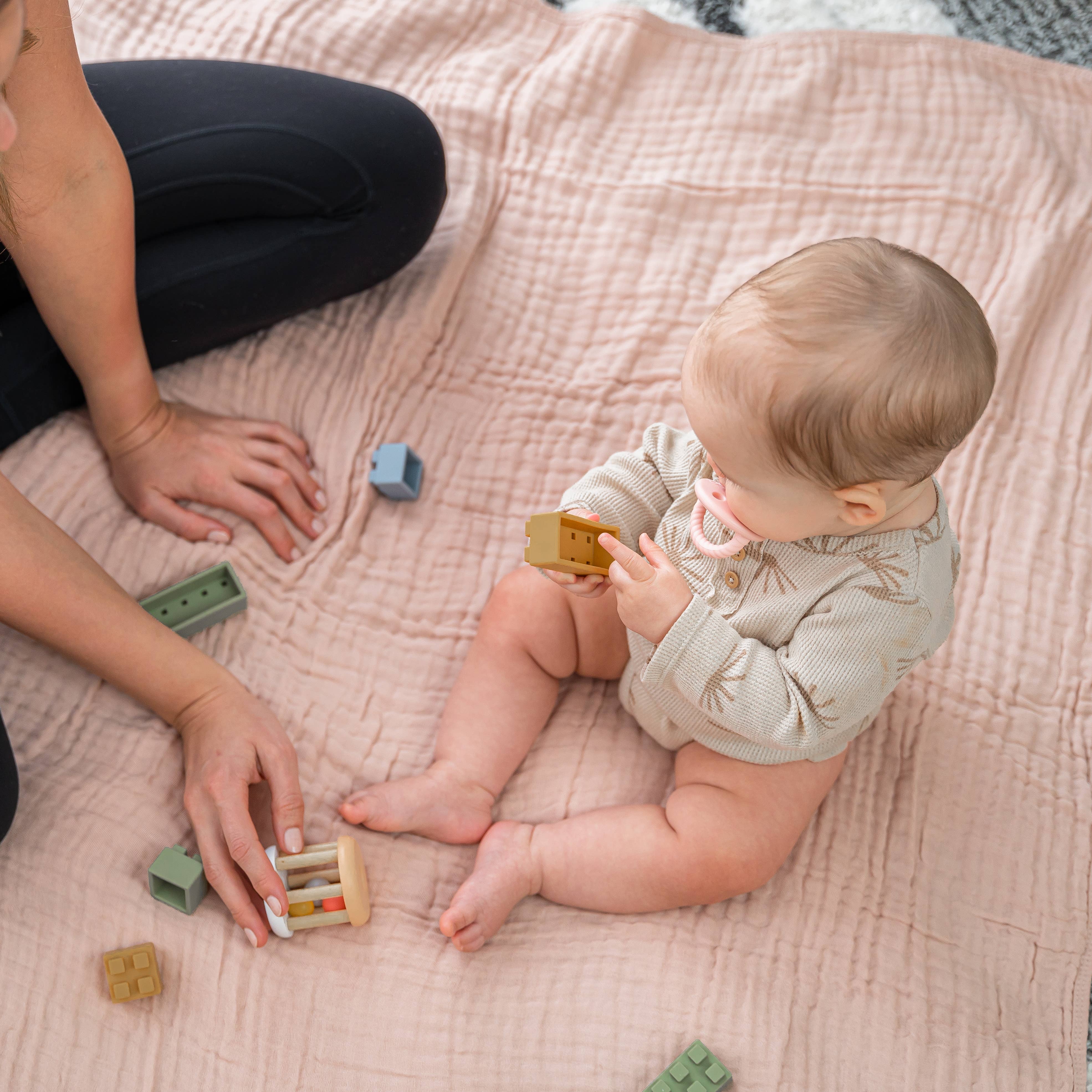 Baby playing with colorful blocks on a soft muslin cotton blanket, enjoying cozy and comfortable moments with a parent.