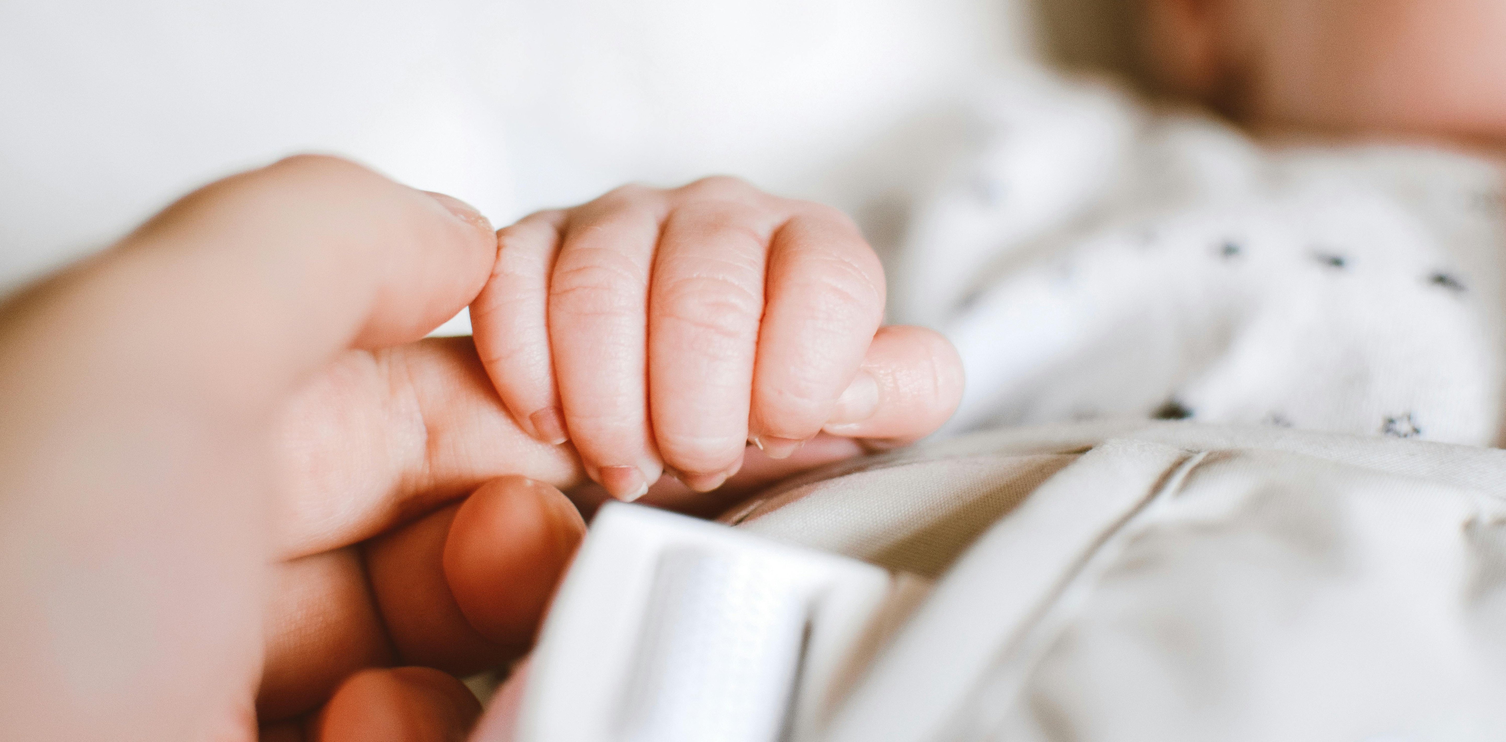 A close-up of a baby's hand grasping an adult finger, showcasing a tender moment of connection.