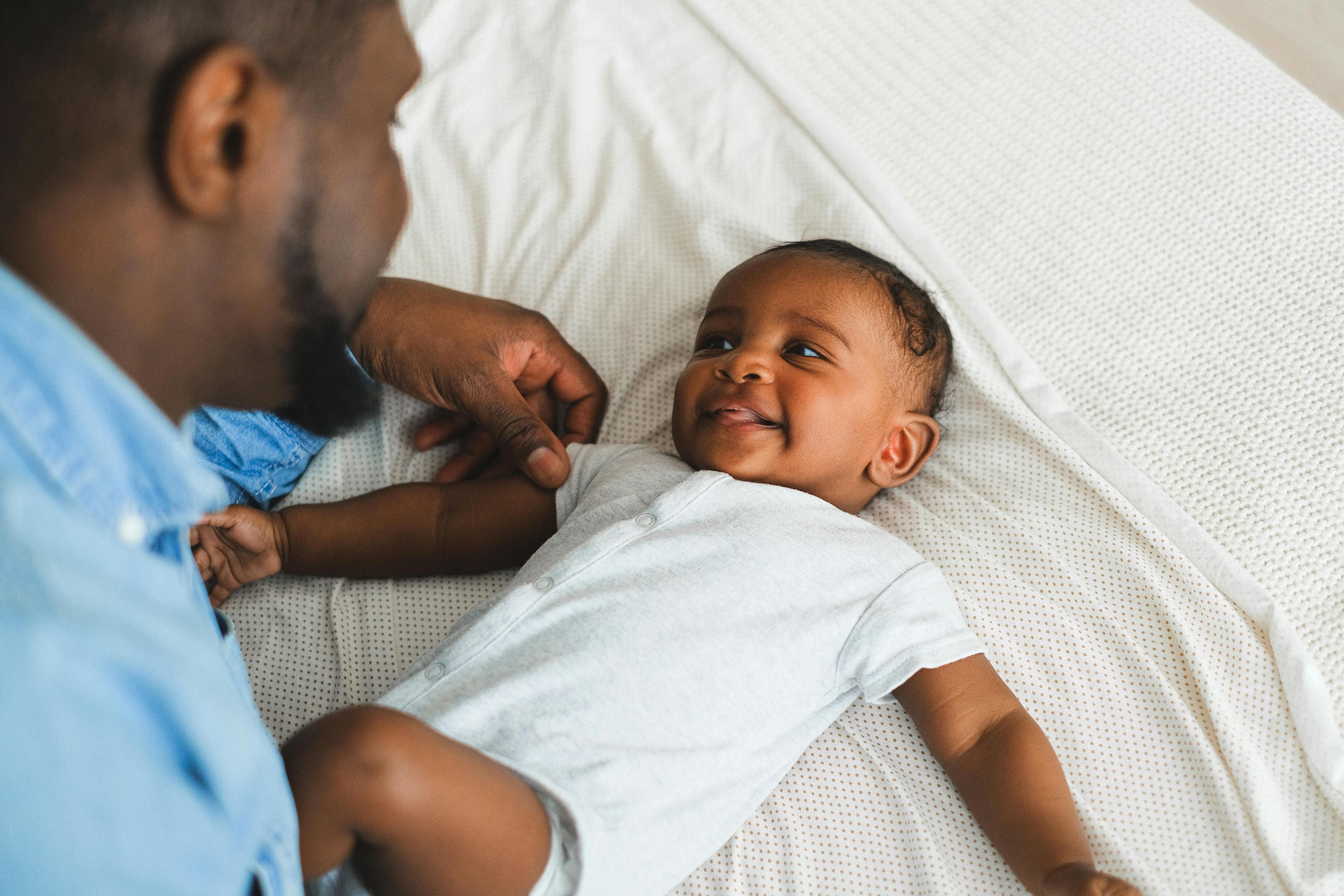 A joyful moment between a father and his smiling baby on a bed, showcasing their loving bond.