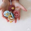 A hand holding assorted Itzy Ritzy natural rubber pacifiers in various colors, perfect for babies 6-18 months.
