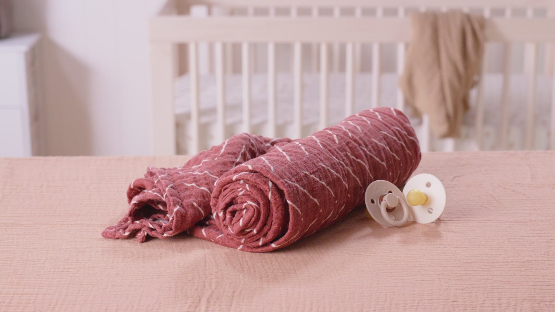 Itzy Ritzy Breastfeeding Boss™ rolled nursing cover and pacifier on a soft surface, perfect for multitasking parents.